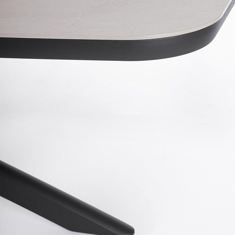 Close up of ISACCO outdoor dining table edge showing a light gray sintered stone top and dark graphite powder coated aluminum base