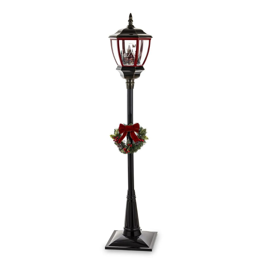 Fekete állólámpa piros lámpásfejjel, téli falu jelenettel és koszorúval – teljes nézet, fehér háttér.
