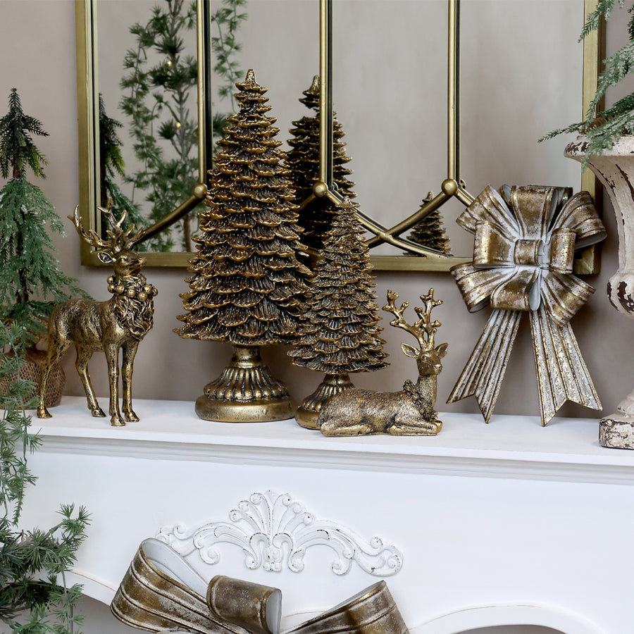 Rustic gold Art Ferro display with metal trees and deer beside a large antique gold bow on a mantel.