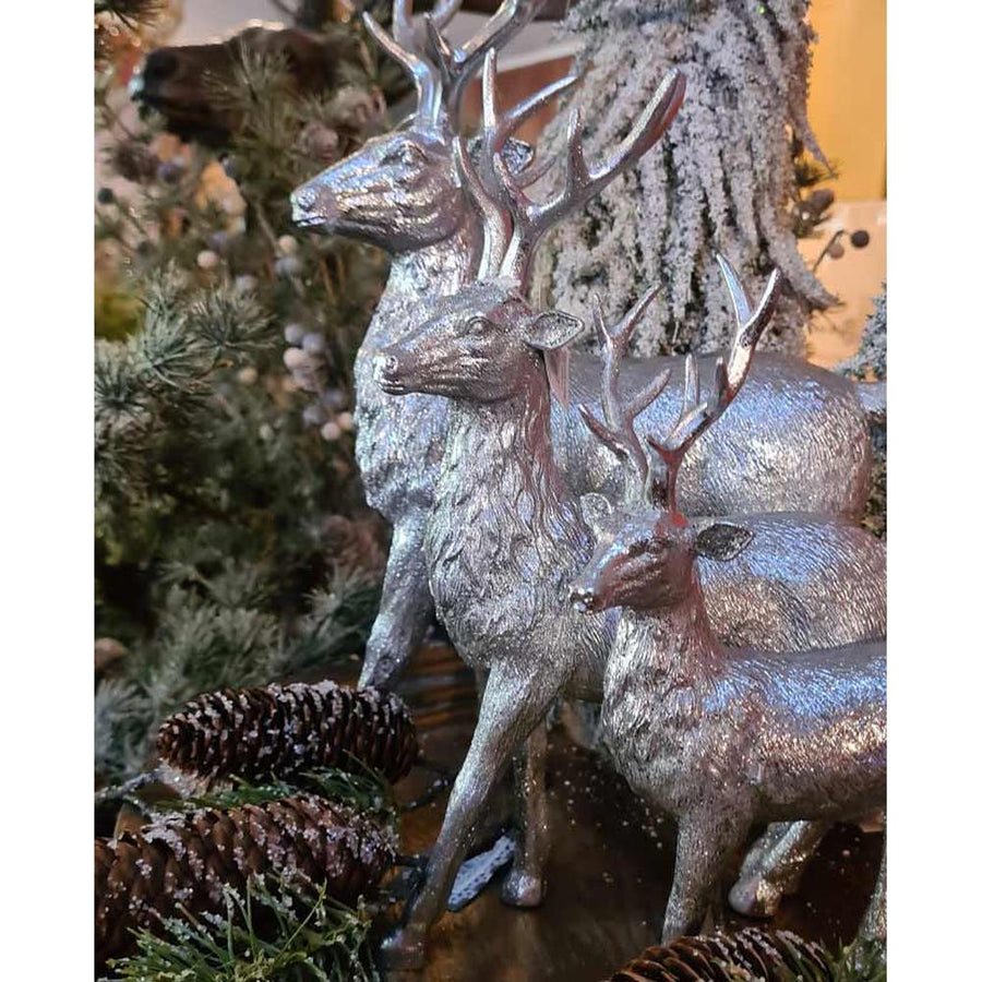 Glamour stílusú, 36 cm magas, ezüst színű karácsonyi szarvas figura többféle méretben, fenyők és tobozok között