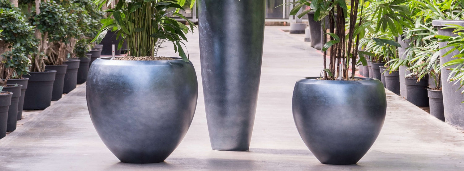 BAQ Metallic design kaspók Matt Ice Blue színben – modern beltéri kaspók fémes felülettel, kézzel készített kivitelben, zöld növényekkel ültetve.