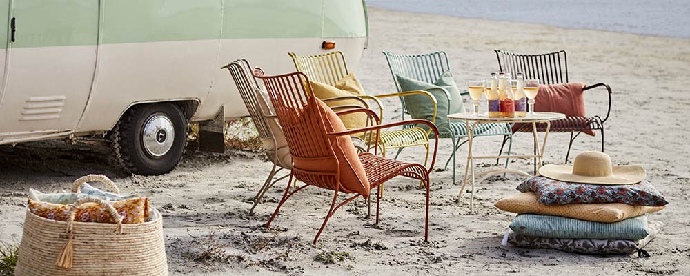 Retro stílusú, fém kerti székek a tengerparton, lakókocsival.