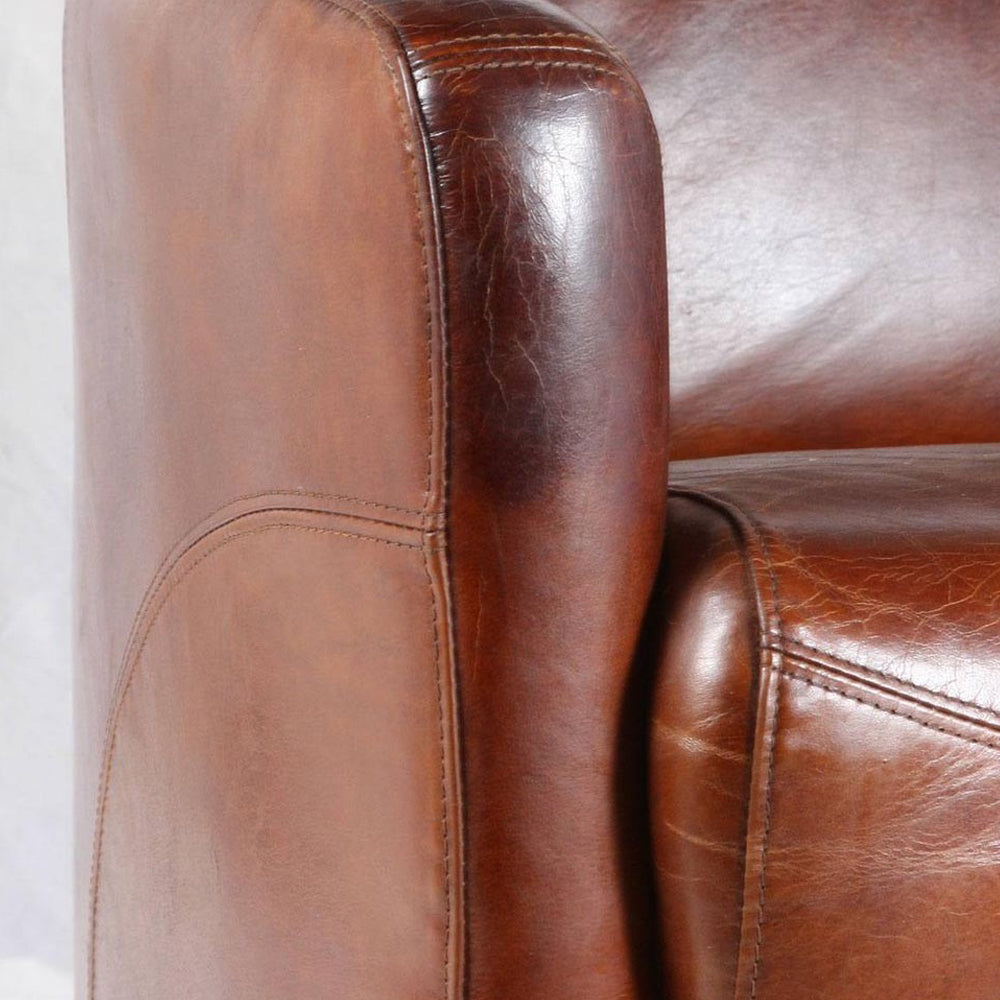 Közeli kép a vintage bőrkanapé karfájáról és varrásairól, patinás dohánybarna bőr felülettel.