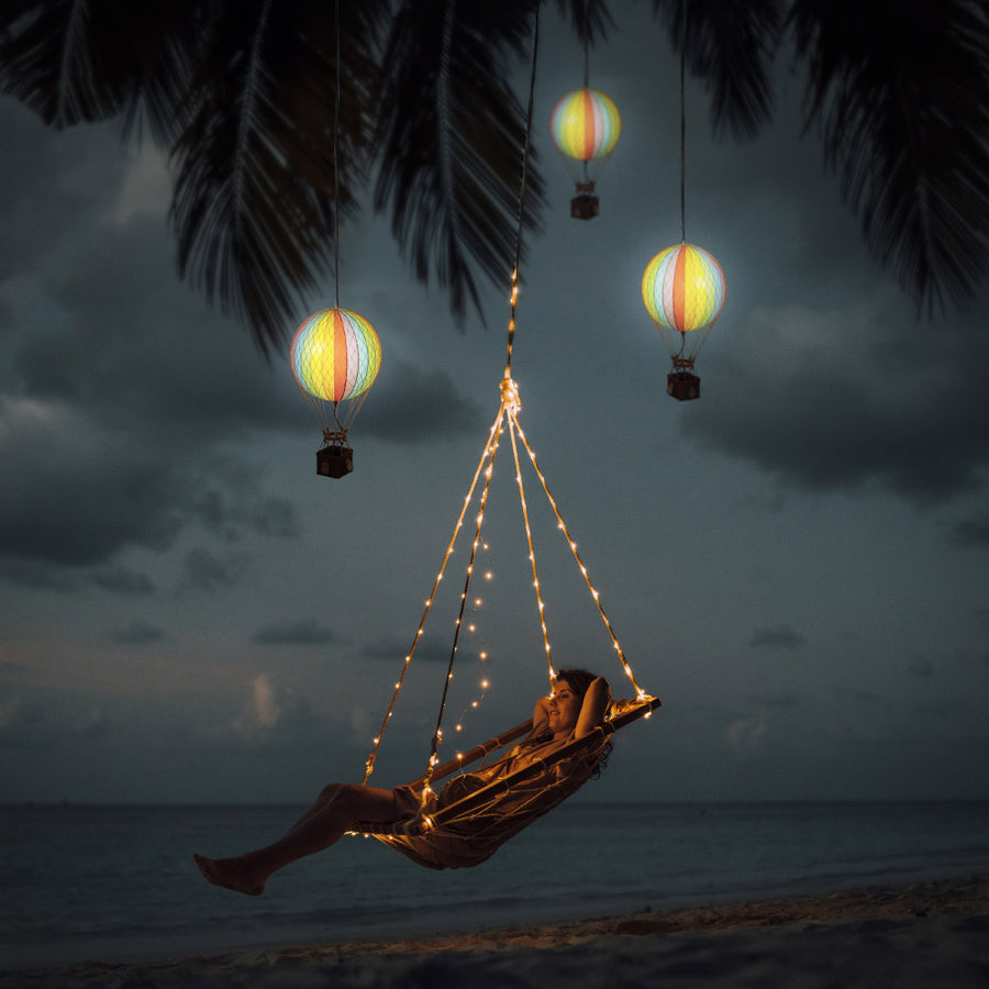 Tengerparti függőfotel szivárványszínű LED-es hőlégballonokkal díszítve.