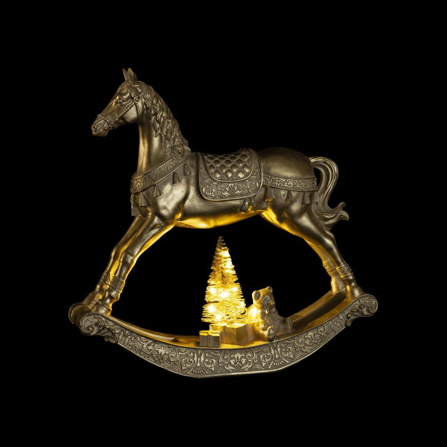 Arany karácsonyi hintaló LED-világítással, sötét háttér előtt, világító fenyővel és ajándékdíszekkel.