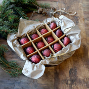 Vintage stílusú meggybordó karácsonyfadíszek díszdobozban, rusztikus papírral és fenyőággal körülvéve