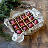 Vintage stílusú meggybordó karácsonyfadíszek díszdobozban, rusztikus papírral és fenyőággal körülvéve