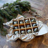 Vintage stílusú antik olívazöld karácsonyfadíszek díszdobozban, fenyőág és rusztikus papír környezetben