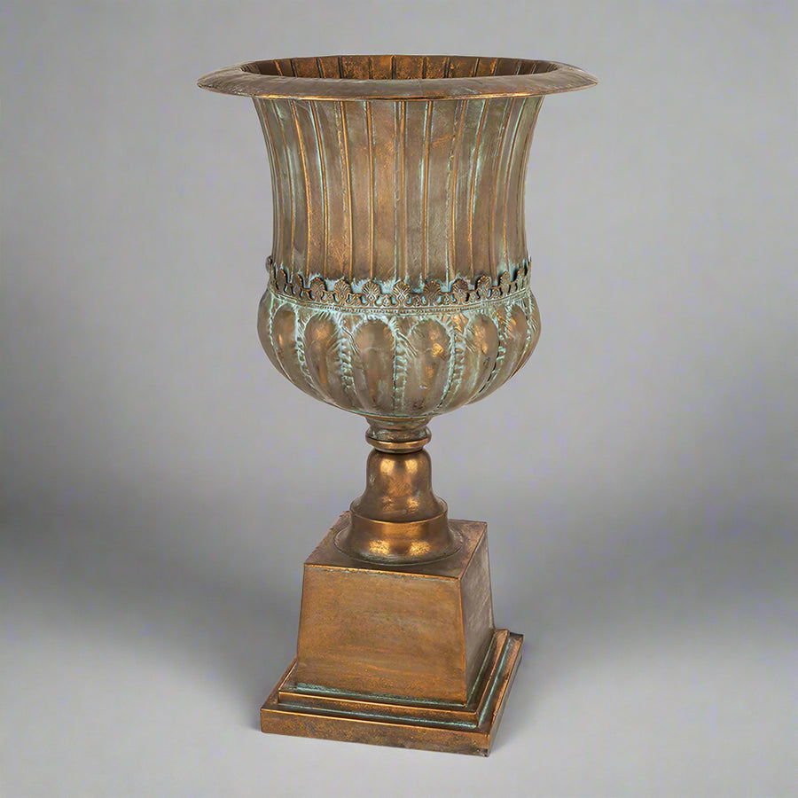 Antique Metals klasszikus stílusú, antik rézszínű fém kaspó teljes magasságban, patinázott felülettel és díszes talapzattal.