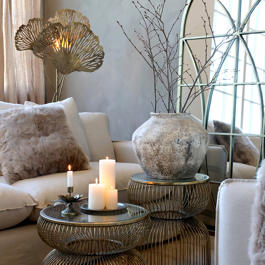 Krémszínű antik váza letisztult nappali enteriőrben, üvegasztalon elhelyezve.