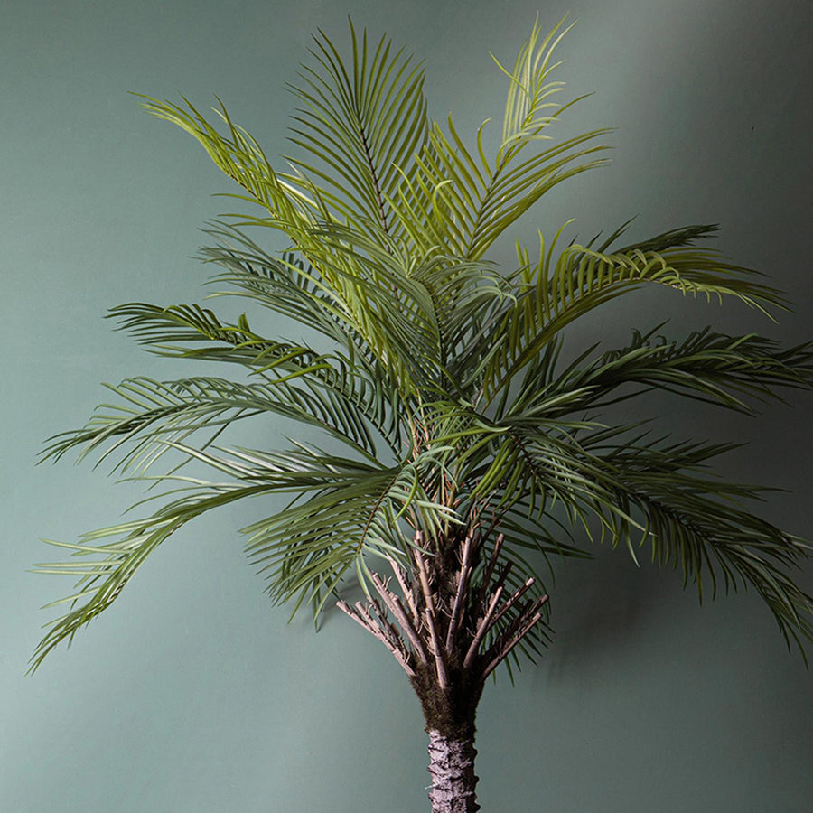 Dekoratív Areca zöld mű pálmafa beltéri elhelyezésben, zöld háttér előtt.