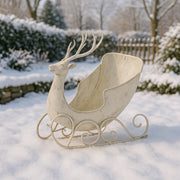 Antikolt krém színű, szarvasfigurás fém dekor szán téli kertben, havas háttérrel, nappali fényben, rusztikus karácsonyi hangulatot idézve.