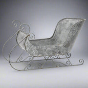 Teljes nézetű fém szán dekoráció stúdiókörnyezetben, antik szürke színben, klasszikus formákkal.