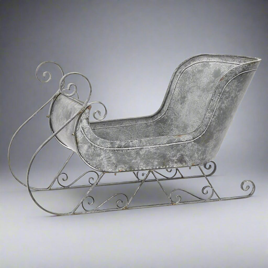 Teljes nézetű fém szán dekoráció stúdiókörnyezetben, antik szürke színben, klasszikus formákkal.