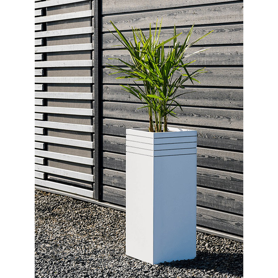 Modern kültéri környezetben elhelyezett fehér Line-Up kaspó zöld levelű növénnyel, fa falburkolat mellett