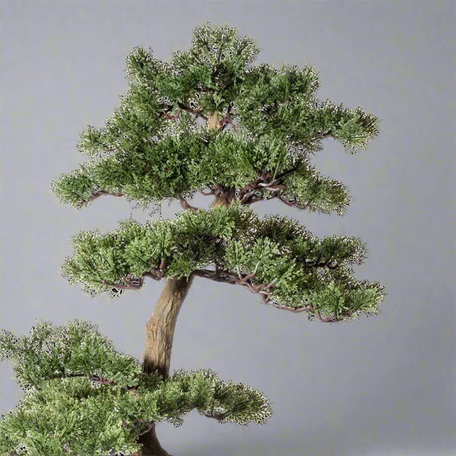Zöld színű, mű cédrus bonsai fa, fekete színű ovális műanyag cserépben.
