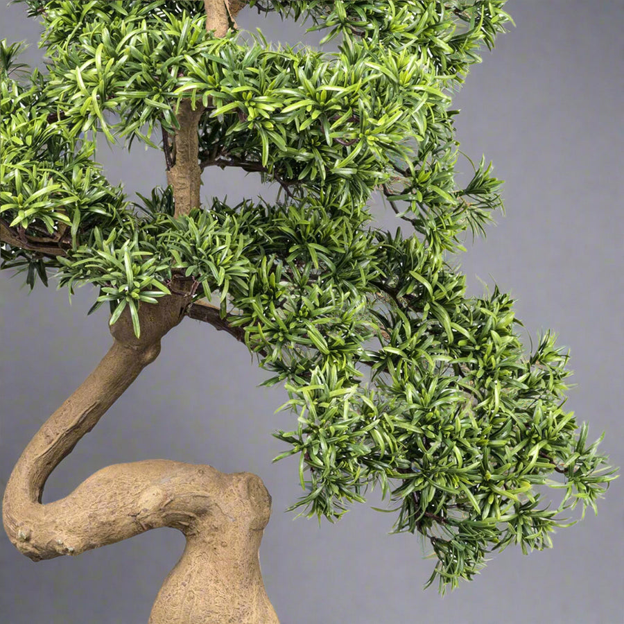 Mű kőfenyő bonsai fa, fekete színű műanyag cserépben.