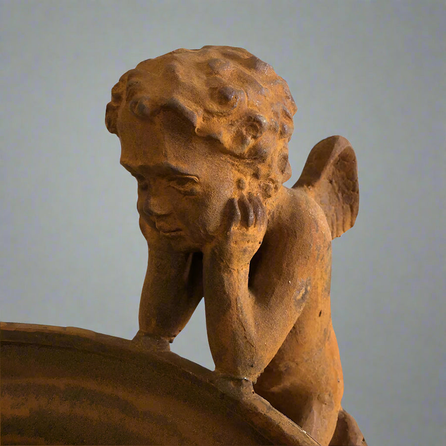 Könyöklő puttófigura részlet a Château Jardin öntöttvas kaspóról, finoman kidolgozott antik felülettel és klasszikus bájjal.