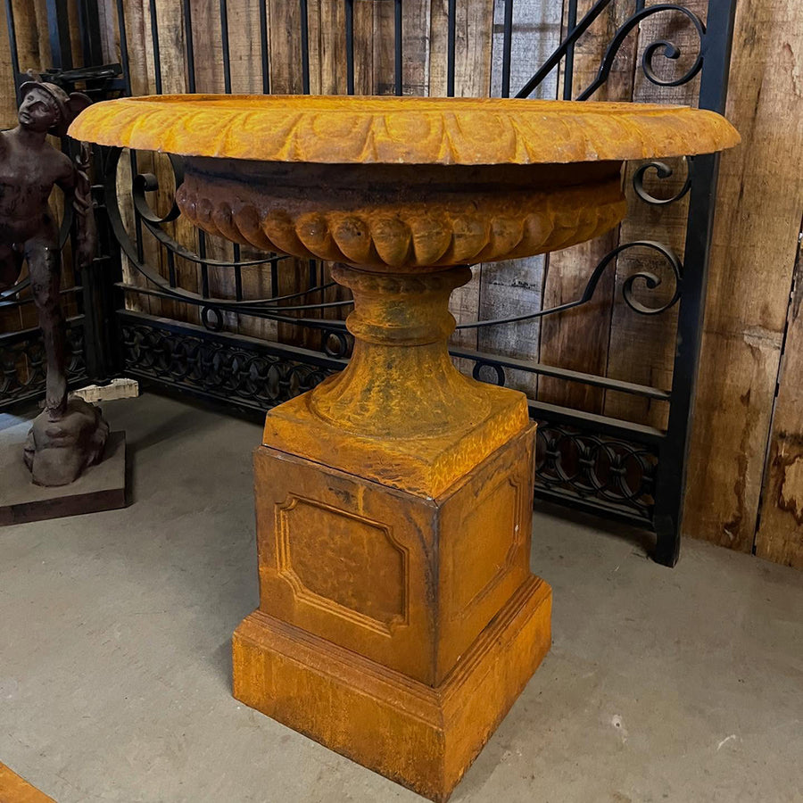 Château Jardin antikolt öntöttvas díszkaspó posztamensen, rozsdaszínű felülettel, műhelybelsőben elhelyezve, klasszikus részletekkel.