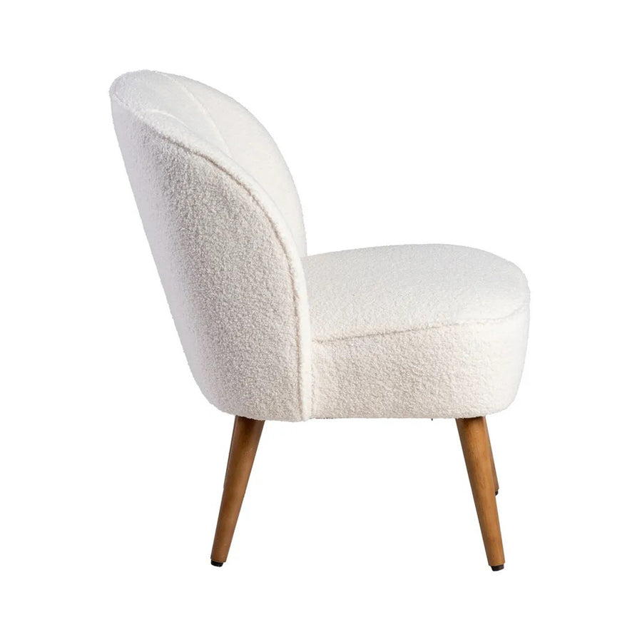 Bézs klub fotel oldalnézetből, ívelt háttámlával és puha ülőfelülettel.