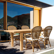 Mézbarna rattan székek kültéri elrendezésben, fa étkezőasztallal kombinálva.