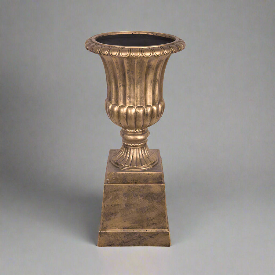 Elegáns aranyszínű England kaspó posztamenssel stúdióvilágításban, szürke háttéren.