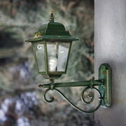 Ferroluce Gorizia klasszikus kültéri falilámpa felszerelve egy ház falára, zöld patinás alumínium testtel és ívelt fém konzollal.