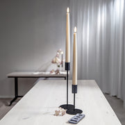 Két bézs LED vacsoragyertya fekete gyertyatartóban, világító lánggal, világos asztalon, mellette távirányító és díszvirág.