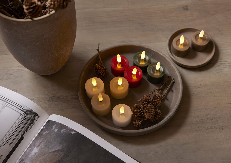 Többszínű Star Trading LED teamécsesek tálcán elrendezve, köztük zöld, piros, bézs és fehér változatok, természetes dekorációval és tobozokkal díszített, hangulatos enteriőrben