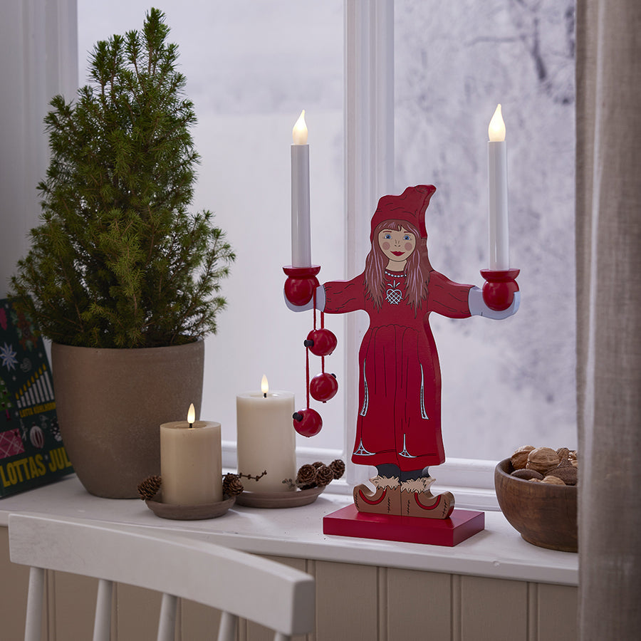 Bézs Star Trading Flow LED gyertyák és piros karácsonyi dísz a téli ablakpárkányon, havas háttérrel – meghitt ünnepi dekoráció az otthonodban.