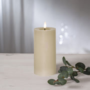 Bézs színű LED oszlopgyertya valódi viaszból, pislákoló lánggal, világos háttér előtt, dekoratív zöld eukaliptuszággal.
