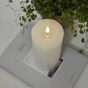 Fehér LED gyertya a Star Trading Flow kollekcióból egy magazinon, növénnyel dekorálva, letisztult enteriőrben.