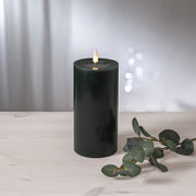 Zöld LED oszlopgyertya valódi viaszból, pislákoló lánggal, világos fa felületen, eukaliptuszlevéllel díszítve.