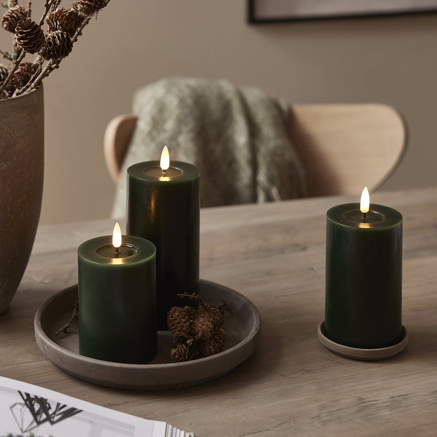Zöld Star Trading LED gyertyák természetes dekorációs környezetben, mécsestartó tálcán, fa és zöld ágakkal.