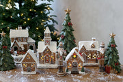 Gingerbread diótörő szett mézeskalácsházakból és zöld dekor fenyőfákból összeállított karácsonyi jelenetben.