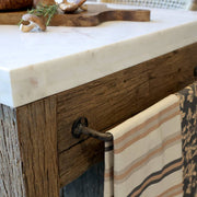 Sötét fém törölközőtartó rúd a Grimaud szervírozóasztal oldalán, textillel dekorálva.