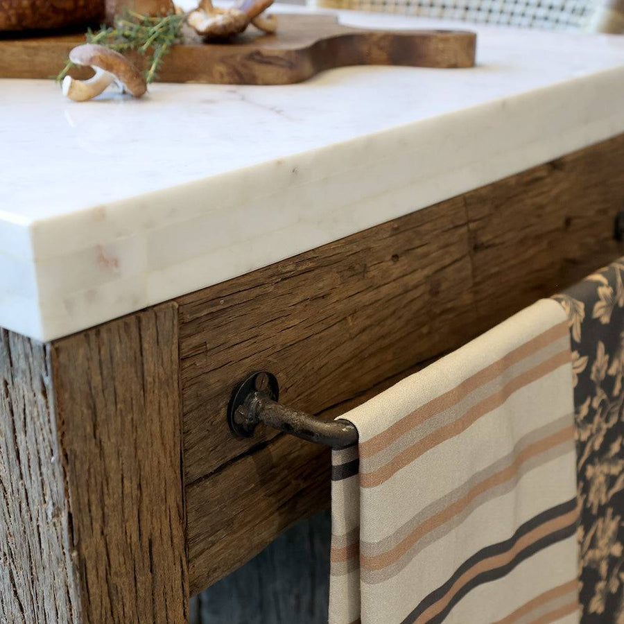 Sötét fém törölközőtartó rúd a Grimaud szervírozóasztal oldalán, textillel dekorálva.