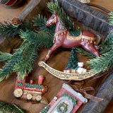 NOÉL bordó karácsonyi hintaló figura ünnepi enteriőrben, fenyőágak között