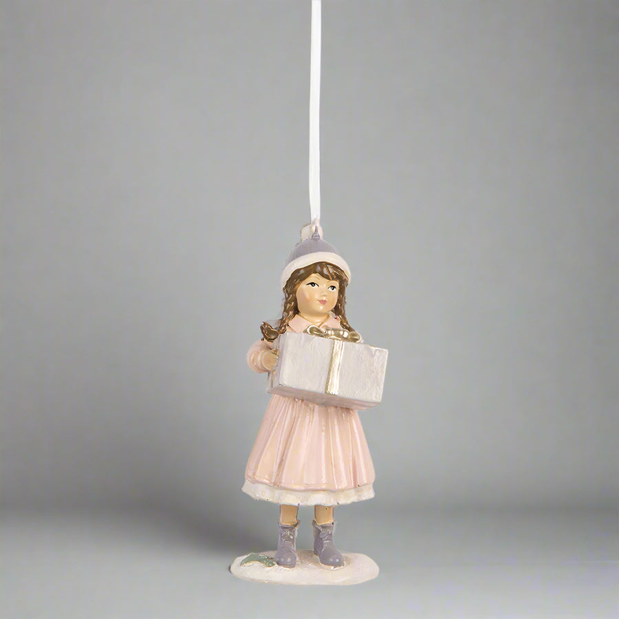 Nosztalgikus hangulatú pink téli kislány karácsonyfadísz közelről, könyvvel a kezében.