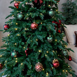 Piros és zöld Heritage üvegdíszekkel, masnikkal és meleg fényű fényfüzérrel feldíszített karácsonyfa egy nappaliban.
