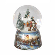 Karácsonyi zenélő-forgó hógömb, téli házikó előtt hóembert építő gyerekekkel.