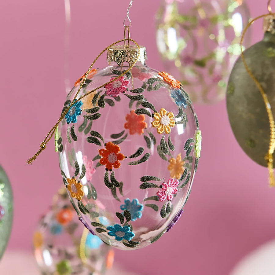 Plasztikus virágokkal díszített, függeszthető húsvéti üvegtojás.