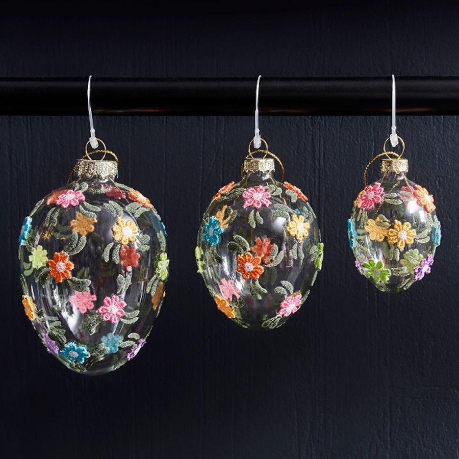 Plasztikus virágokkal díszített, függeszthető húsvéti üvegtojás.