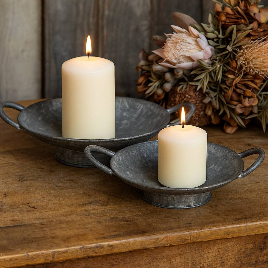Két különböző méretű JUNKER bádog tál gyertyákkal, rusztikus hangulatú enteriőrben, szárított növénydekorral.