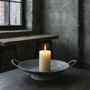 JUNKER szürke bádog tál égő gyertyával, ipari stílusú enteriőrben, nyers falakkal és fa paddal a háttérben.