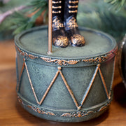 A NOÉL zenélő diótörő dobformájú zöld talapzata arany díszítéssel