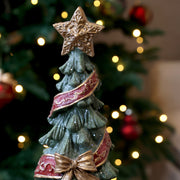NOÉL dekor karácsonyfa aranyszínű, mintás csúcsdísze, piros szalagdíszítése és masnija közelről.