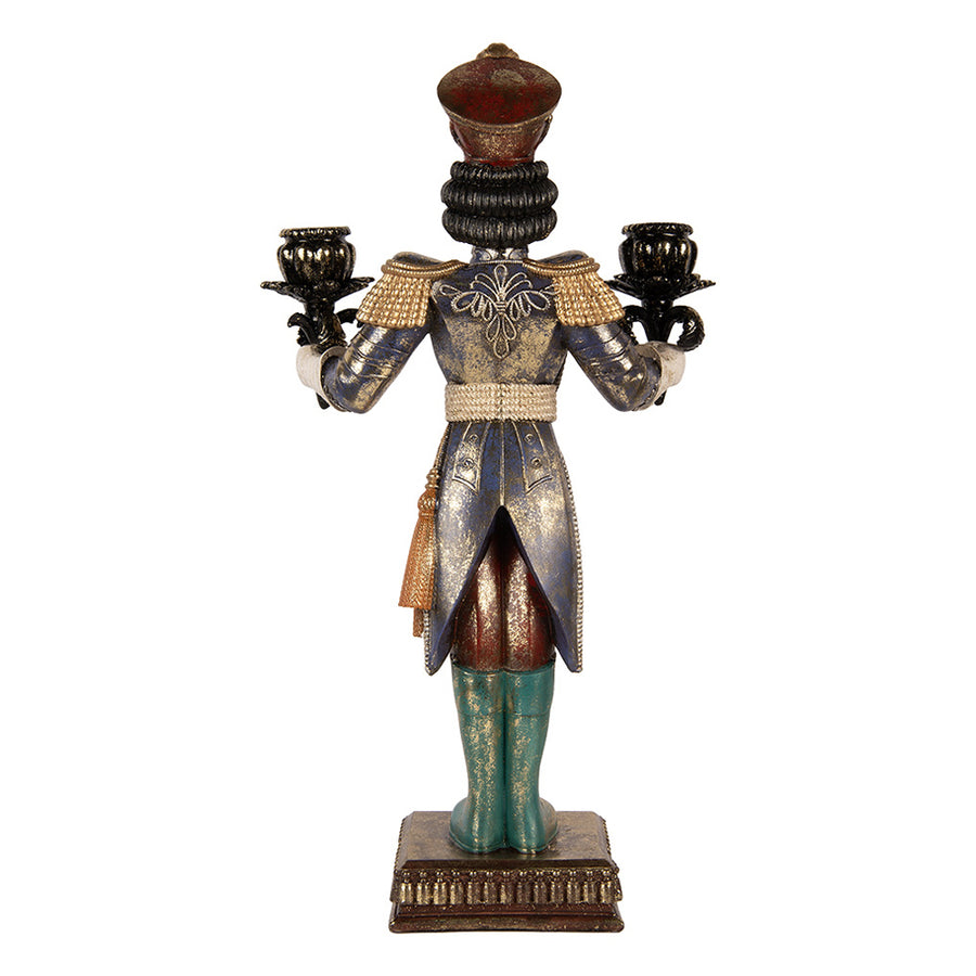 A Nutcracker diótörő figura hátulnézetből, aranymintás sötétkék kabáttal, bordó nadrággal, zöld csizmával és két gyertyatartóval.