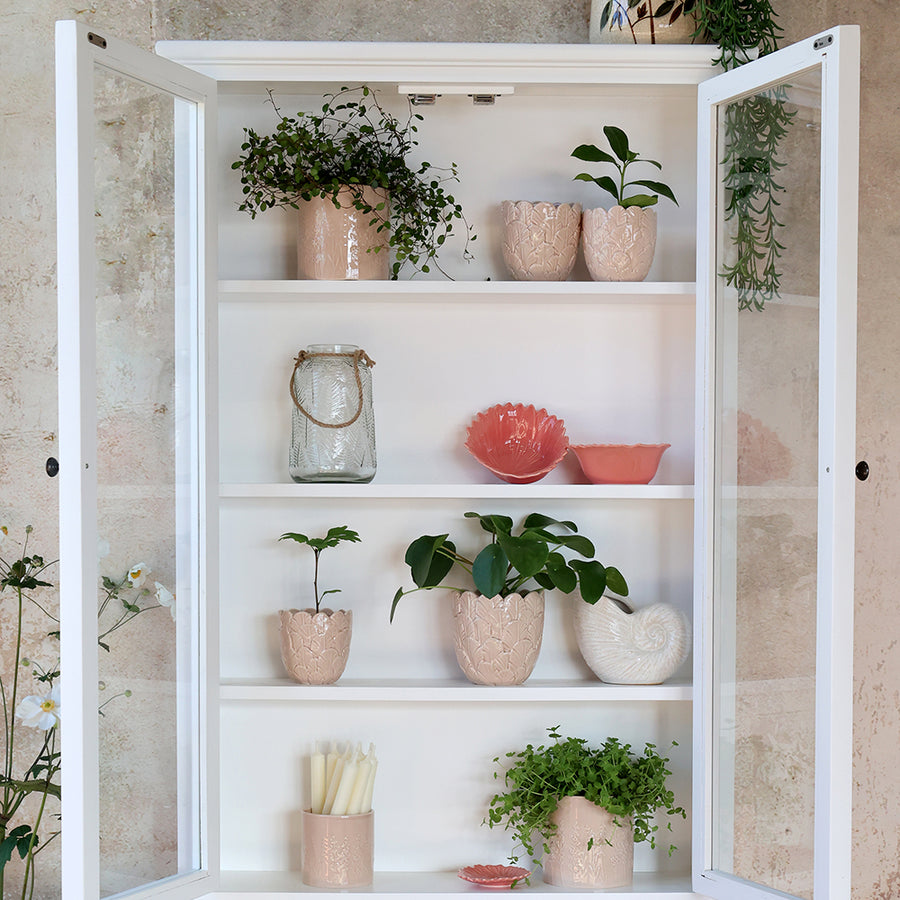 Az Old French fehér faliszekrény nyitott ajtókkal, növényekkel és gyertyákkal díszített belső polcokkal.