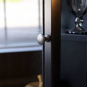Kerek fém fogantyú a vitrines szekrény üvegajtaján, elegáns antikolt kivitelben.